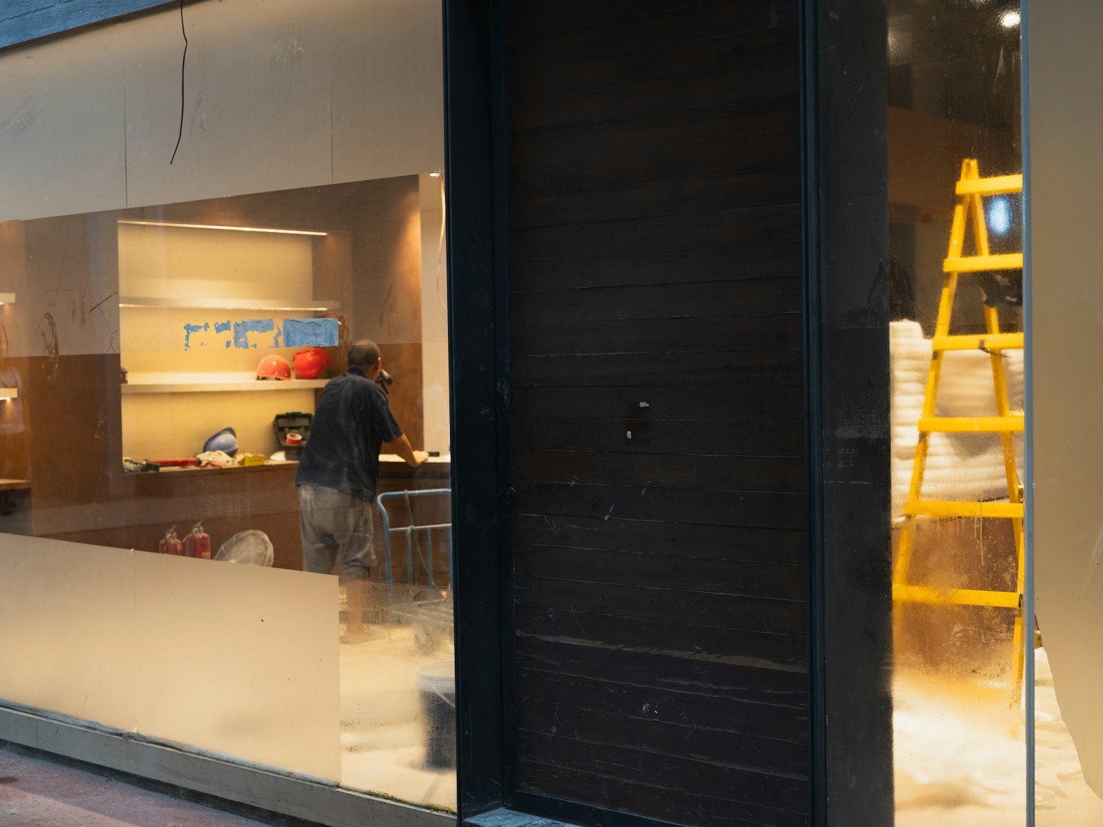 Locale commerciale svuotato e in ristrutturazione con una scala gialla e un operaio al lavoro