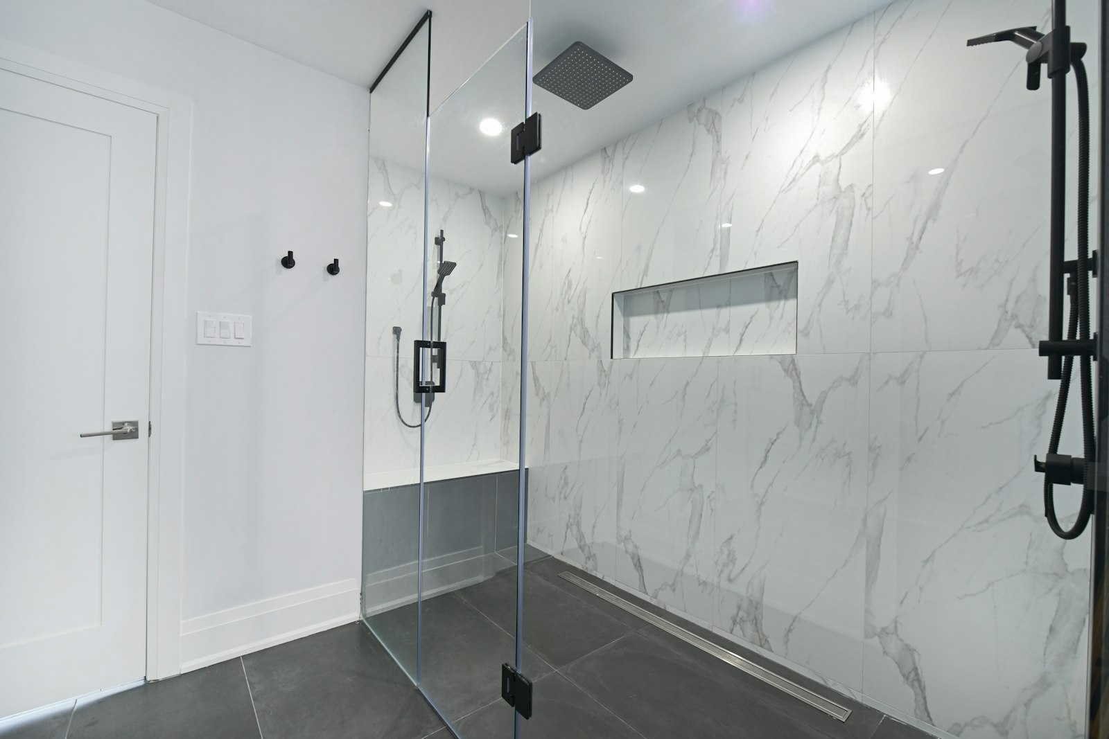 Bagno moderno con doccia a filo pavimento, box in vetro e rivestimento in marmo