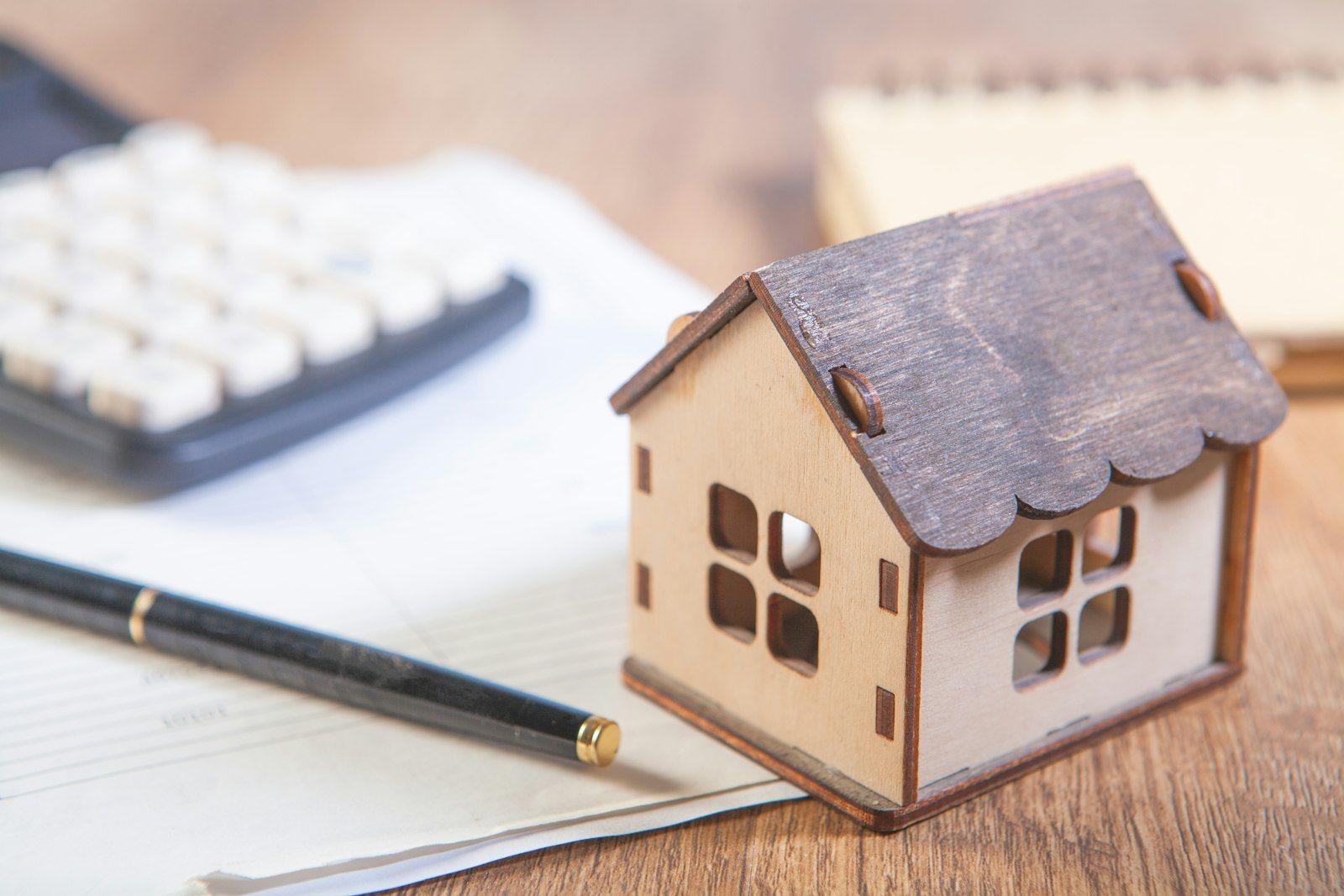 Modellino di una casa con calcolatrice e penna sulla scrivania, per pianificare la richiesta
