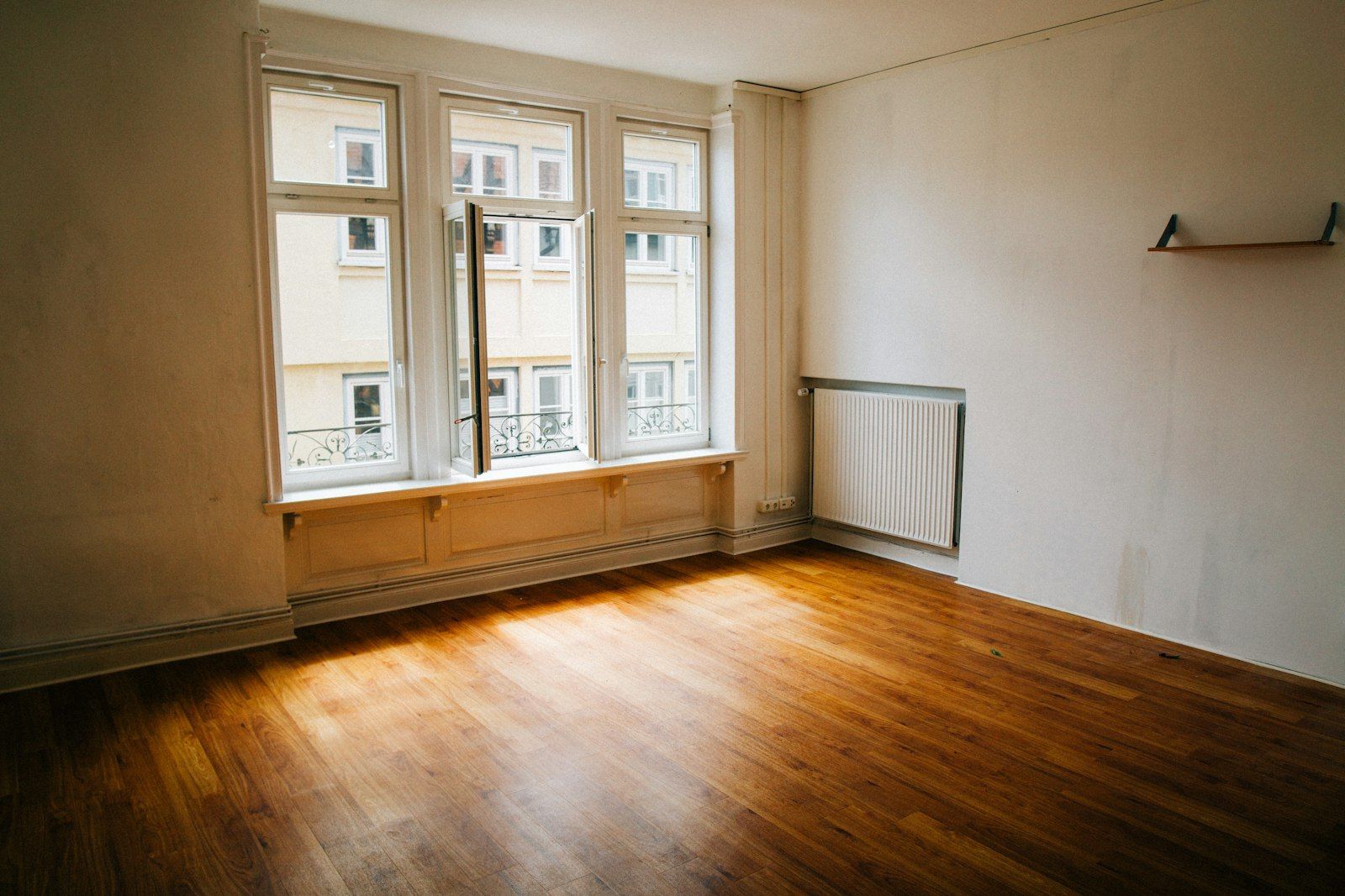 Stanza vuota con pavimento in legno e grande finestra, pronta per la ristrutturazione