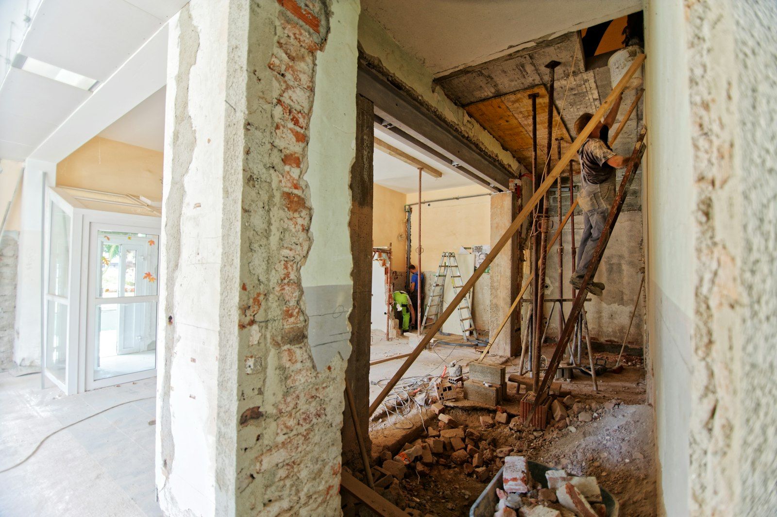 Operaio su una scala all'interno di una stanza in ristrutturazione con intonaco grezzo